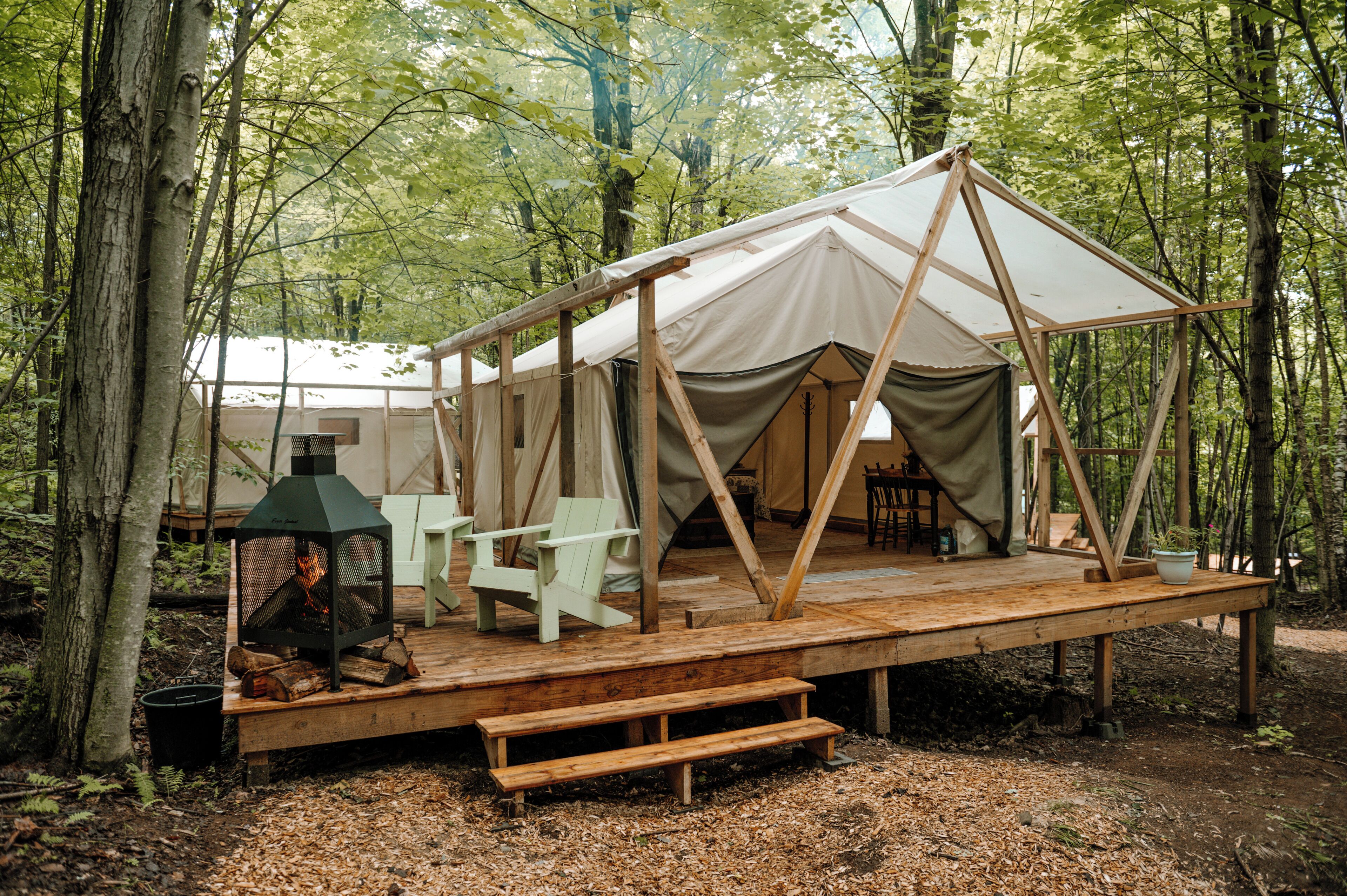 Une tente dotée d’une terrasse en bois, de deux chaises, d’un foyer et d’une table.