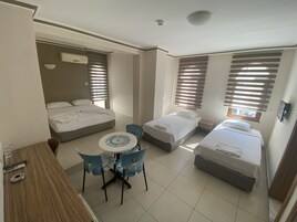 Quarto de hotel com uma cama, uma cama adicional, uma mesa com cadeiras e uma janela com persianas.
