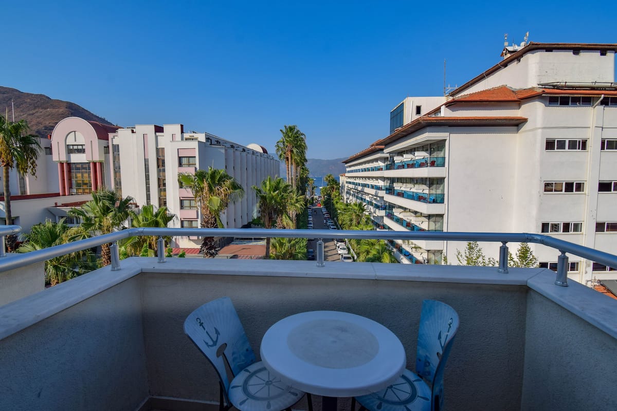 A balcony with a table and chairs, overlooking a street with buildings and palm trees.
