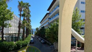 A hotel corridor with a view of parked cars, palm trees, and a building with balconies. - Astoria Life Hotel (Marmaris)
