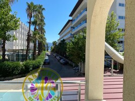 Corredor de hotel com vista para carros estacionados, palmeiras e um edifício com sacadas.