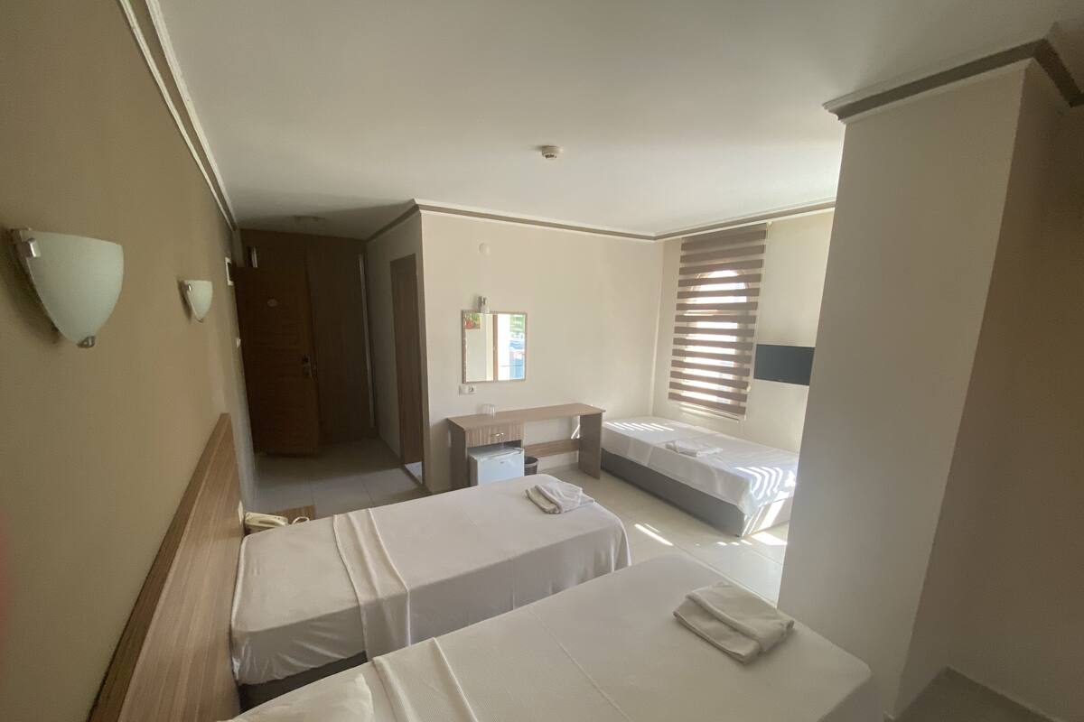 A hotel room with two beds, a small desk, a mirror, and a window with blinds.