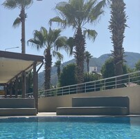 Área de piscina com palmeiras e montanhas ao fundo.