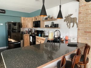 A modern kitchen with a central island, wooden cabinets, and a black refrigerator. - Northern Lights- Relax, Unwind, & Enjoy (Two Harbors)