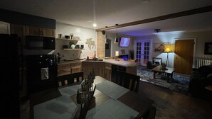 Cocina compacta con armarios de madera, microondas y comedor con mesa y sillas.