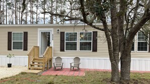 A single-story house with a front porch, a staircase, and two Adirondack chairs.
