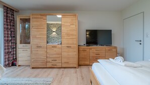 Een slaapkamer met een houten garderobe, een televisie op een dressoir en een bed met een witte deken.