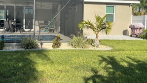 Un patio trasero con piscina, un área de patio techada y una pequeña palmera.