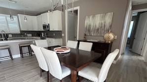 Una cocina moderna con armarios blancos, una mesa de comedor con seis sillas y una isla de cocina con microondas.