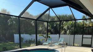 Una piscina al aire libre techada con sillas de descanso y una cerca blanca al fondo.