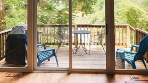 A room with a large sliding glass door leading to an outdoor deck with a table and chairs, a barbecue grill, and a view of trees. - Rest & Recharge, A-frame Cabin on Winery Grounds (Colonial Beach)