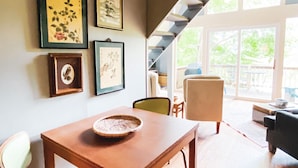 A dining area with a wooden table and chairs, framed artwork on the wall, and a view of the outdoors through large windows. - Rest & Recharge, A-frame Cabin on Winery Grounds (Colonial Beach)