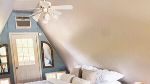 A bedroom with a large bed, a ceiling fan, a nightstand with a lamp, and a door with a window. - Rest & Recharge, A-frame Cabin on Winery Grounds (Colonial Beach)