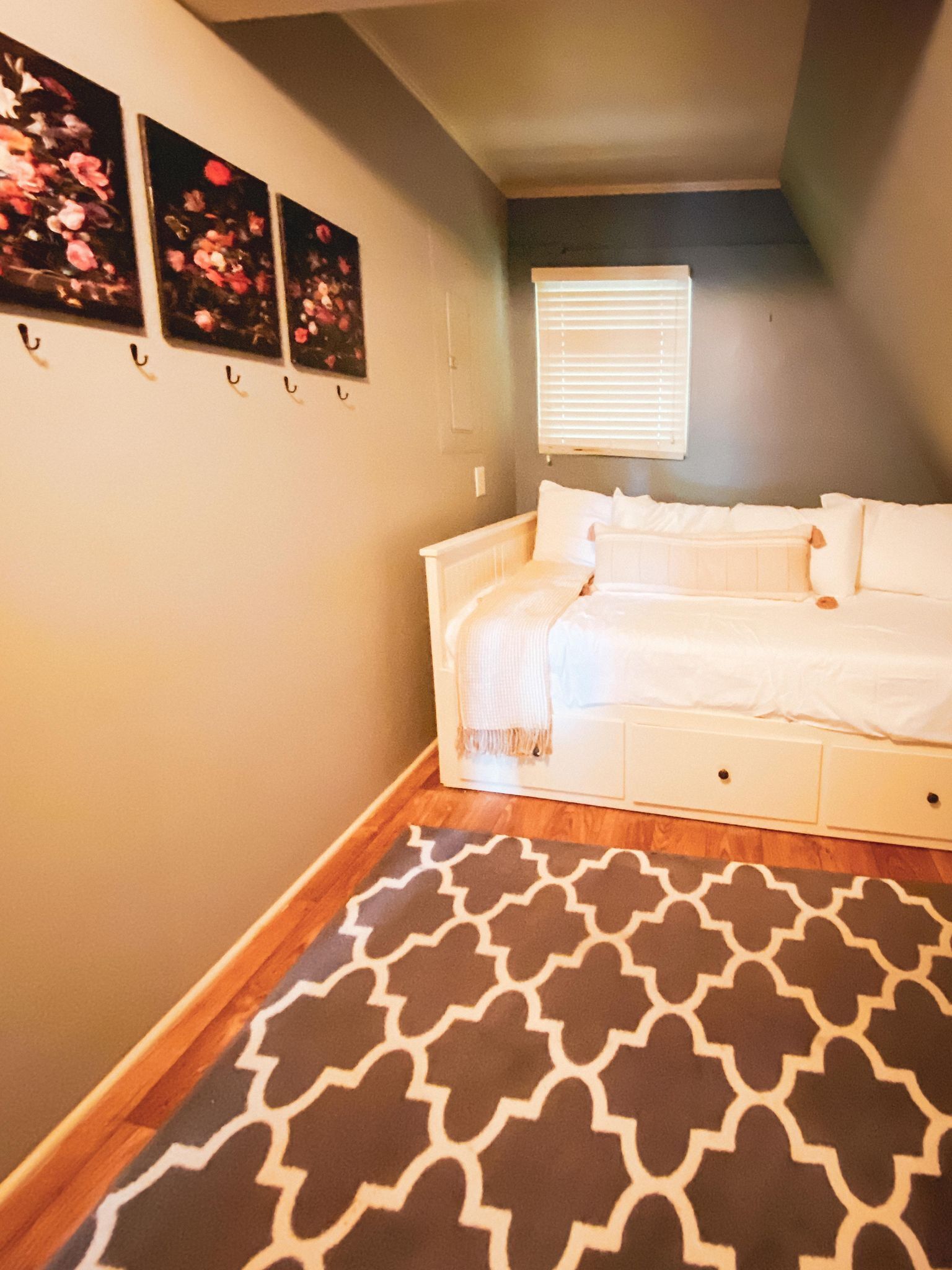 Ein Schlafzimmer mit einem weißen Bett, einem gemusterten Teppich und drei Blumenbildern an der Wand.