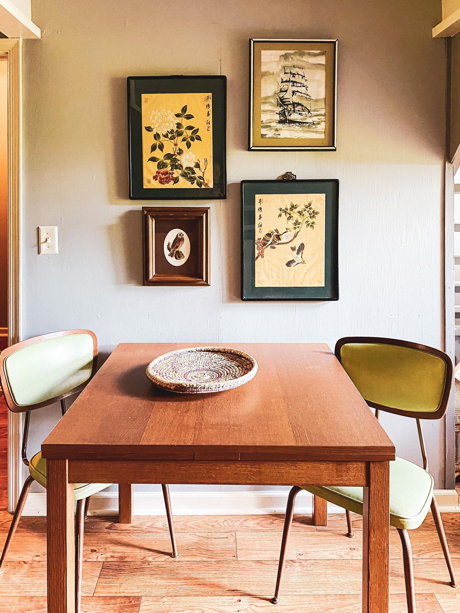 Una mesa de comedor con una cesta tejida, dos sillas y cuadros en la pared.
