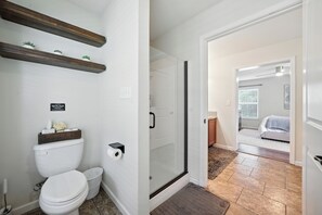 Een moderne badkamer met toilet, douche en een glazen deur naar een slaapkamer.