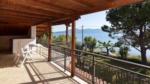 Un espace extérieur abrité, doté d’un plafond en bois, d’une table et de chaises, et offrant une vue sur la mer et les montagnes.