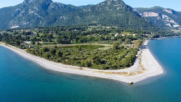Vue aérienne d’une zone côtière avec une plage, une petite île couverte d’une végétation luxuriante et des montagnes en arrière-plan.
