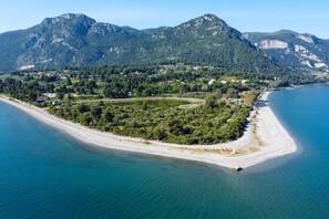 An aerial view of a coastal area with a beach, a small island with dense greenery, and mountains in the background.
