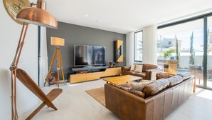 A modern living room with a large flat-screen TV, leather sofa, wooden coffee table, and a floor lamp.