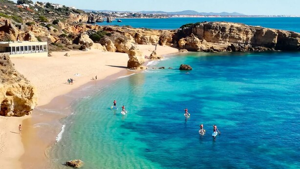 A coastal beach with clear turquoise waters, rocky cliffs, and a sandy shore.
