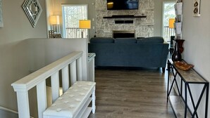 A modern living room with a stone fireplace, a large TV mounted on the wall, a bench, and a wooden floor.