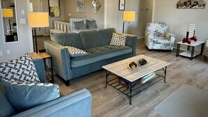 A modern living room with a grey sofa, a patterned armchair, and a coffee table with pet bowls.