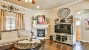 A living room with a fireplace, a large TV, and a sofa. - POOL, Firepit, Gameroom, Great for Families (Lubbock)