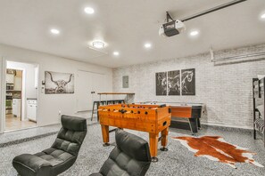 Une pièce comprenant une table de baby-foot, deux fauteuils en cuir, un tapis en peau de vache et un projecteur fixé au plafond.