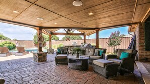 An outdoor patio with wicker furniture, a stone table, and a pool in the background. - POOL, Firepit, Gameroom, Great for Families (Lubbock)