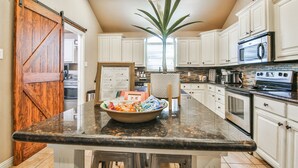 A kitchen with white cabinets, a black granite countertop, a wooden barn door, and a large potted plant. - POOL, Firepit, Gameroom, Great for Families (Lubbock)
