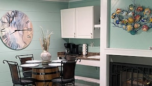 A cozy living room with a round wooden table, four chairs, a large clock, and a fireplace. - The Pelican Post 1 bedroom beach cottage (Carrabelle)