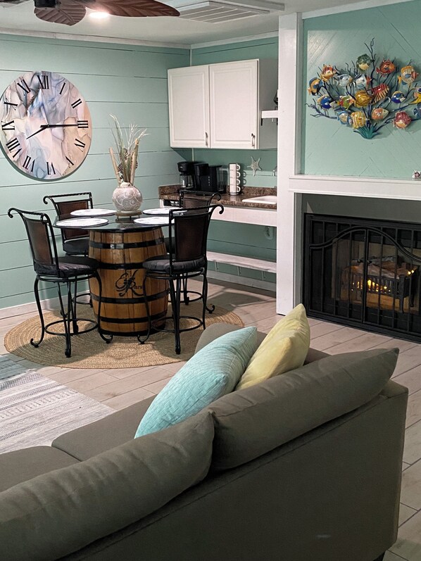 A cozy living room with a round wooden table, four chairs, a large clock, and a fireplace.
