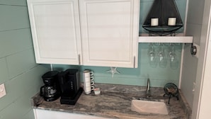 A kitchen with white cabinets, a coffee maker, a sink, and a shelf with wine glasses. - The Pelican Post 1 bedroom beach cottage (Carrabelle)
