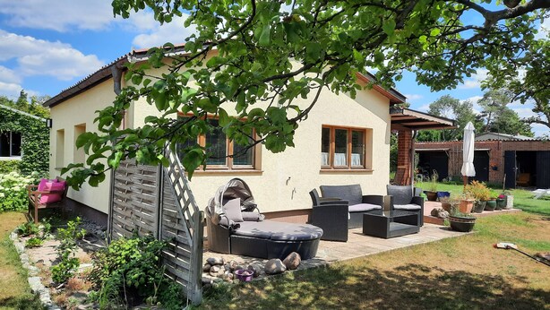 A house with a patio area featuring outdoor furniture, a baby stroller, and a garden with plants and rocks. - Idyllic vacation home on Gorinsee / Wandlitz, 45 min. from the center of Berlin (Wandlitz)