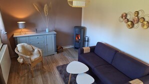 A cozy living room with a blue sofa, a wicker chair, a small white table, a cabinet, and a wood-burning stove. - Idyllic vacation home on Gorinsee / Wandlitz, 45 min. from the center of Berlin (Wandlitz)