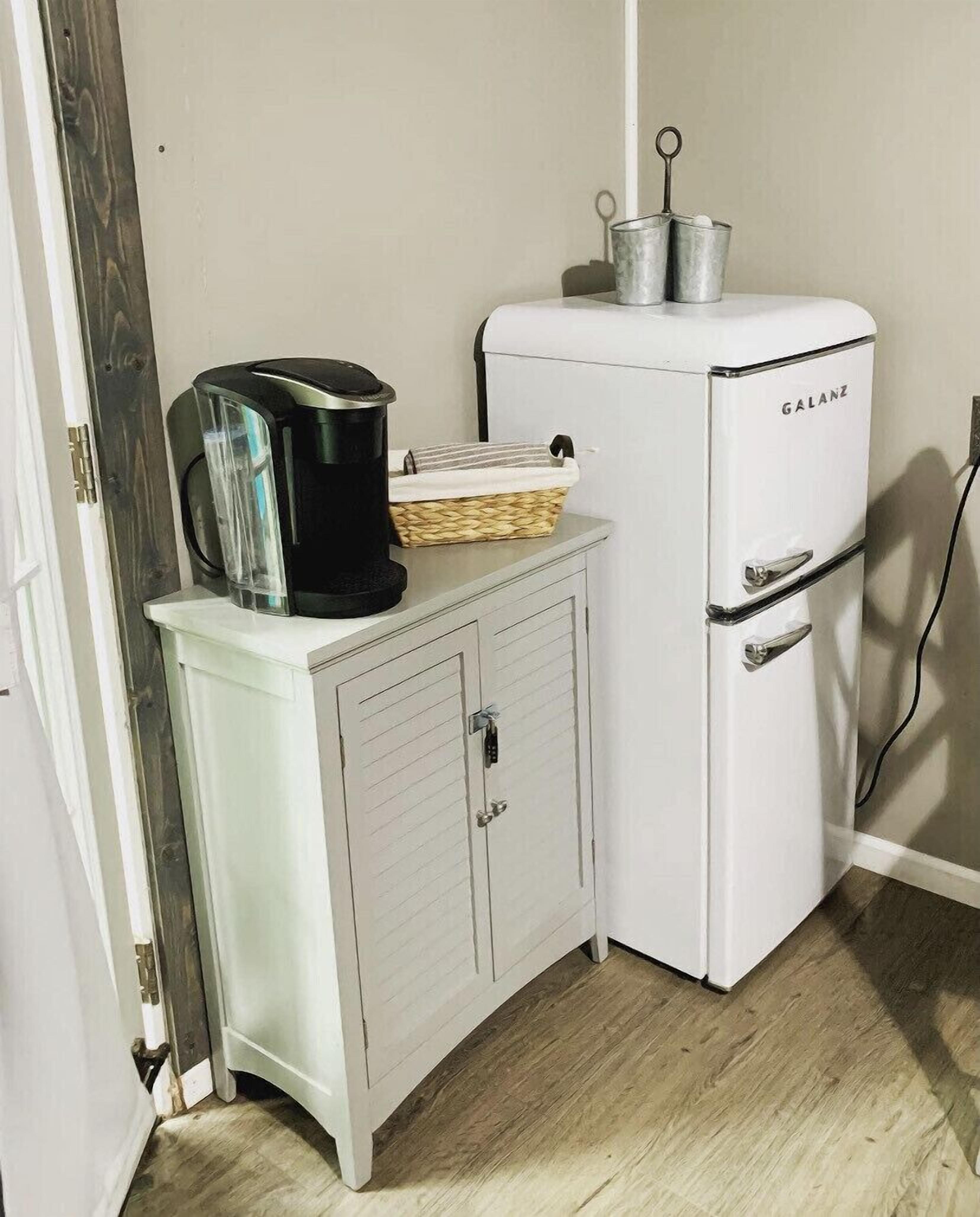 Una kitchenette compacta con un refrigerador blanco Galanz, un mueble blanco pequeño con una cesta y una cafetera negra.