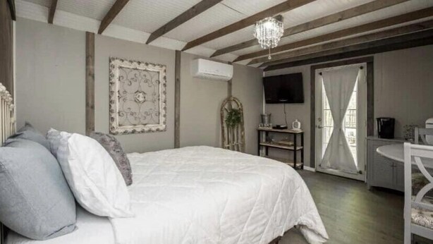 Un dormitorio con cama, candelabro, televisor y ventana con cortinas.