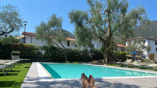 Ein Poolbereich mit Liegestühlen, einem Schwimmbecken und umgebenden Bäumen.