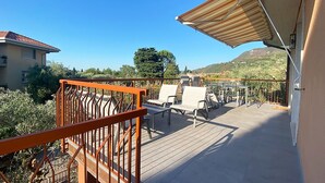 Ein Balkon mit Blick auf eine gebirgige Landschaft, ausgestattet mit einer Holzterrasse, einem Metallgeländer und Gartenmöbeln.