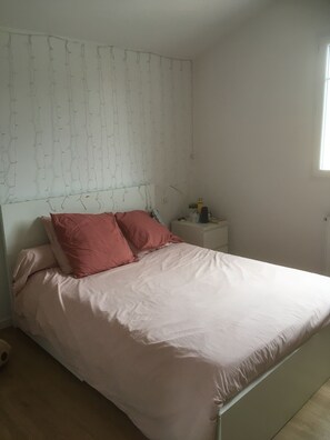 A bedroom with a bed, pillows, a nightstand, and a window.