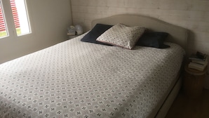 Un lit avec une couvre-lit à motifs, deux oreillers, une table de chevet avec une lampe et une fenêtre avec des stores.