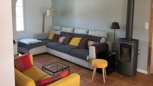 Un salon moderne avec un canapé, un fauteuil jaune, une table basse en verre, une cheminée noire et une lampe.