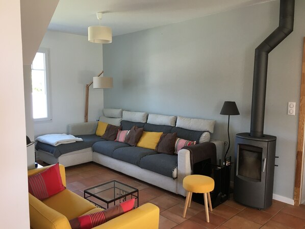 A modern living room with a sofa, a yellow armchair, a glass coffee table, a black fireplace, and a lamp.
