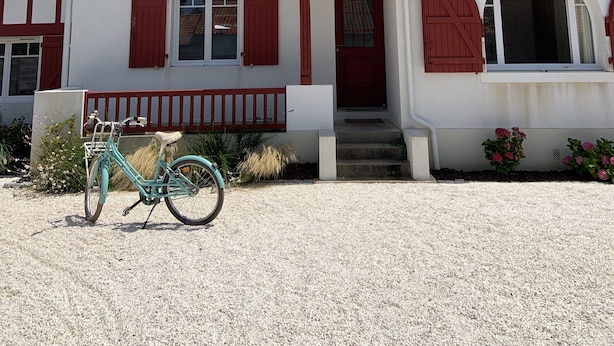 Une maison à deux étages, à la façade rouge et blanche, avec un porche à l’avant et un vélo garé devant.