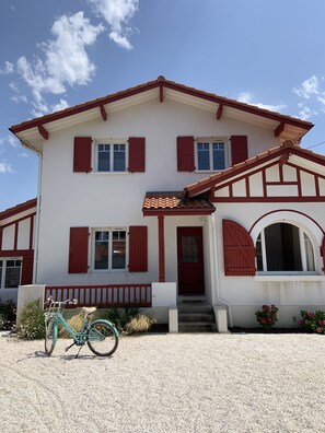 A two-story house with a red and white exterior, a front porch, and a bicycle parked in front.