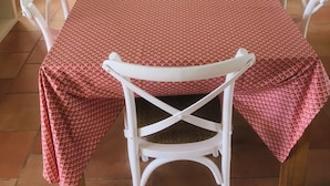 Un coin repas avec une table dressée pour quatre personnes, entourée de chaises blanches, dans une cuisine aux meubles blancs et dotée d’une fenêtre.