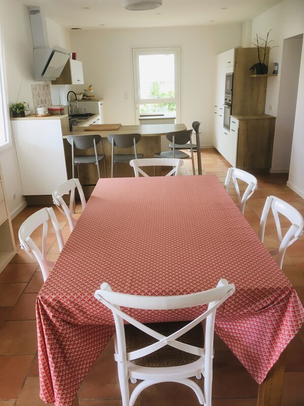 A dining area with a table set for four, surrounded by white chairs, in a kitchen with white cabinets and a window.