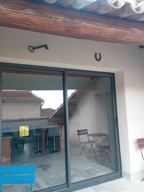 A room with a sliding glass door leading to an outdoor area with a table and chairs. - LE PASSAGE 2 (Montaren-et-Saint-Médiers)