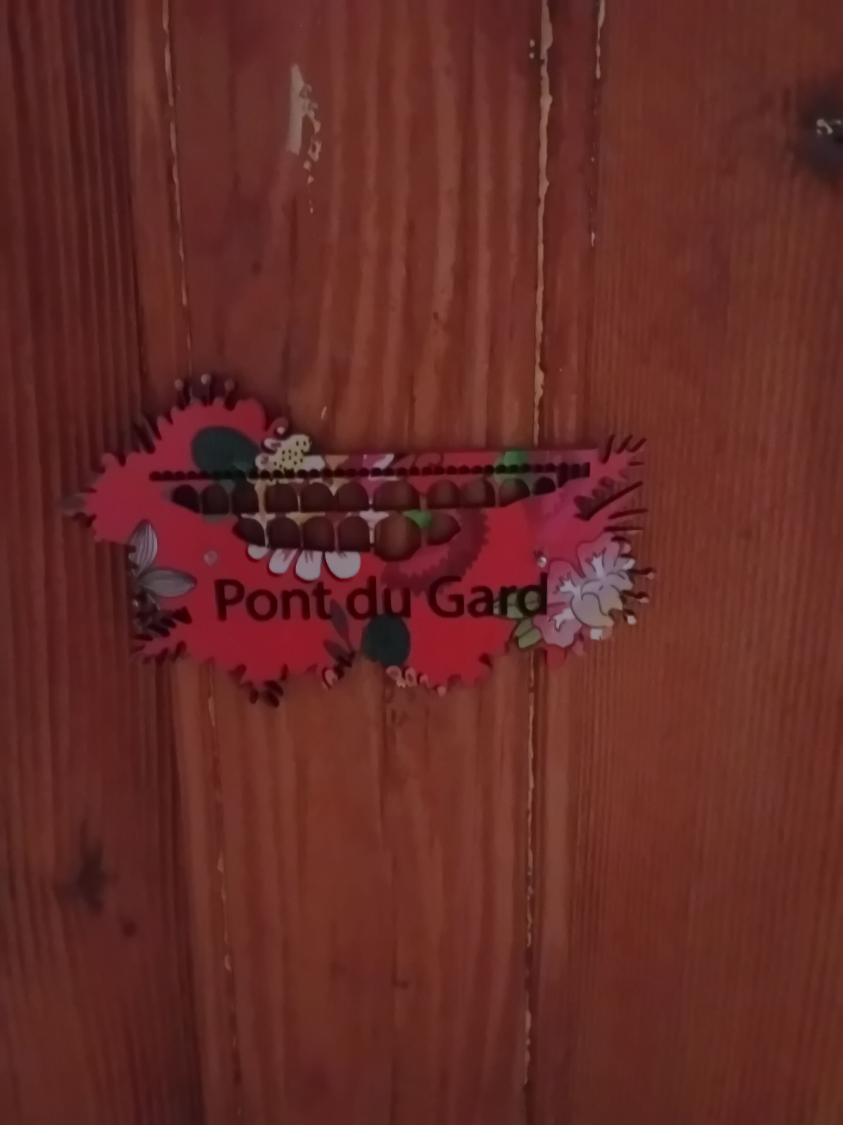 Een houten deur met een decoratief metalen handvat, versierd met een bloemmotief en de tekst 'Pont du Gard'.
